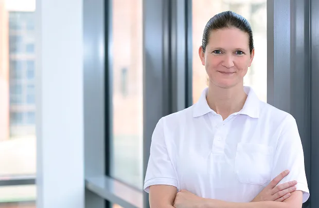 Porträt einer Frau mit verschränkten Armen vor einem Fenster im Büro.