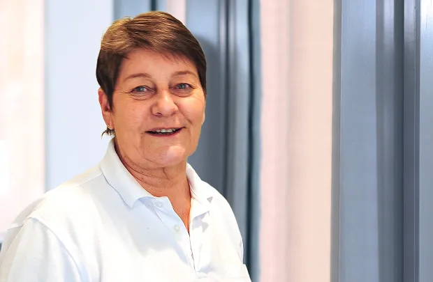 Porträt einer lächelnden Frau mit kurz geschnittenen Haaren vor hellem Hintergrund.